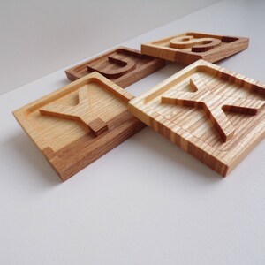 May include: Four wooden blocks with the letters S, U, Y, and K carved into them. The blocks are made of light brown wood with a natural grain pattern.
