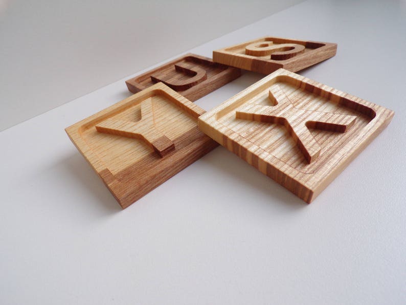 May include: Four wooden blocks with the letters S, U, Y, and K carved into them. The blocks are made of light brown wood with a natural grain pattern.