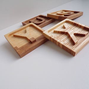 May include: Four wooden blocks with the letters Y, U, K, and S carved into them. The blocks are made of light and dark wood and have a natural finish.