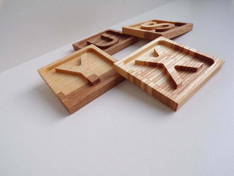 May include: Four wooden blocks with the letters Y, U, K, and S carved into them. The blocks are made of light and dark wood and have a natural finish.