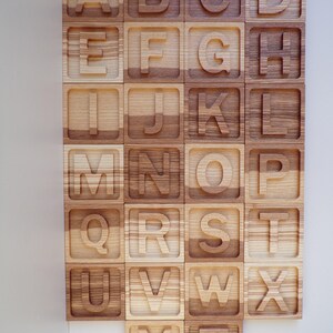 May include: Wooden alphabet blocks with each letter carved into a separate block. The blocks are arranged in alphabetical order and are made of light brown wood.
