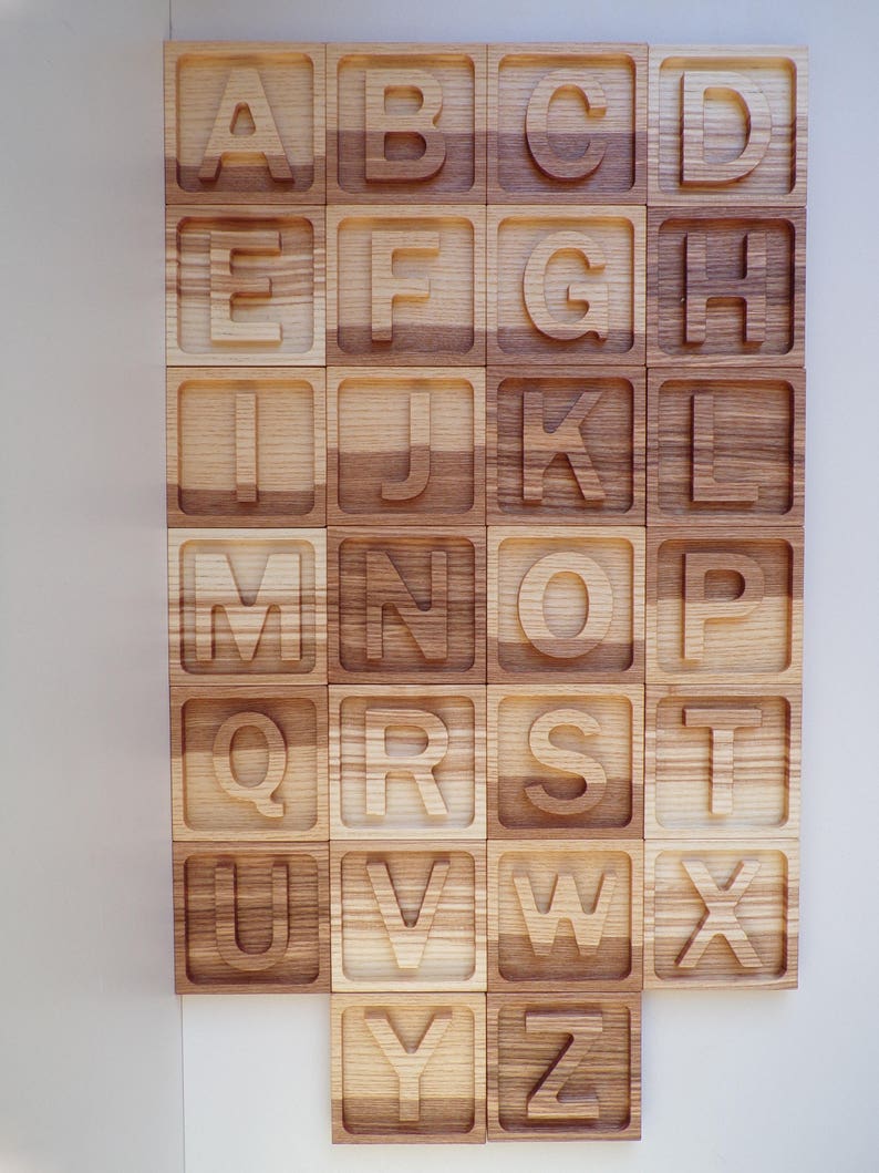 May include: Wooden alphabet blocks with each letter carved into a separate block. The blocks are arranged in alphabetical order and are made of light brown wood.
