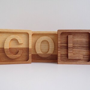 May include: Three wooden blocks spelling out the word "COOL" in all capital letters. Each block is made of two different types of wood, creating a unique two-toned effect.