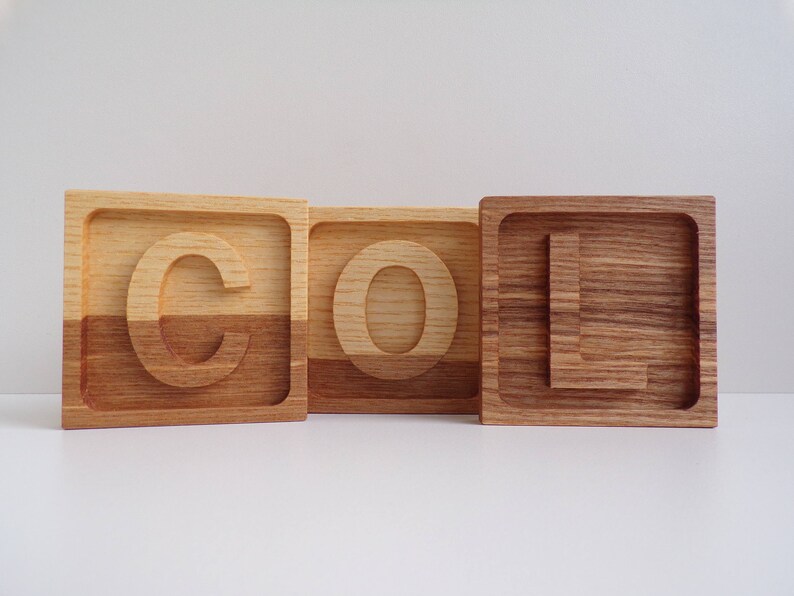 May include: Three wooden blocks spelling out the word "COOL" in all capital letters. Each block is made of two different types of wood, creating a unique two-toned effect.