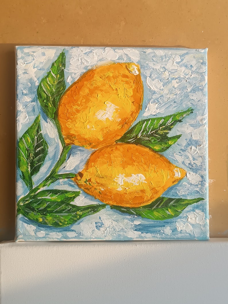 May include: A painting of two yellow lemons with green leaves on a blue and white background.