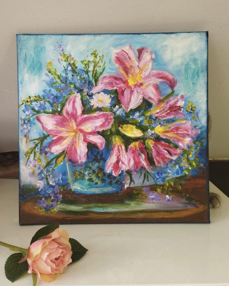 May include: Oil painting of a floral arrangement featuring pink lilies and blue wildflowers in a blue vase. The artwork is on a square canvas with a light blue background. A pink rose lies in the foreground.
