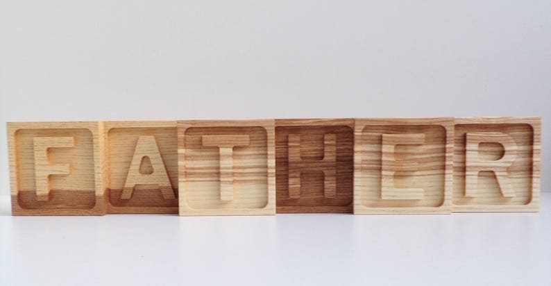 May include: Wooden blocks spelling out the word "FATHER" in all capital letters. Each block is a different shade of brown wood.