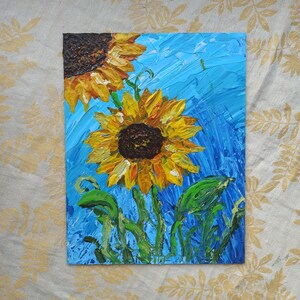 K&ouml;nnte beinhalten: Ein Gem&auml;lde von zwei Sonnenblumen mit gelben Bl&uuml;tenbl&auml;ttern und braunen Zentren vor einem blauen Hintergrund. Die Sonnenblumen sind mit dicken Farbschichten gemalt, was ihnen ein strukturiertes Aussehen verleiht.