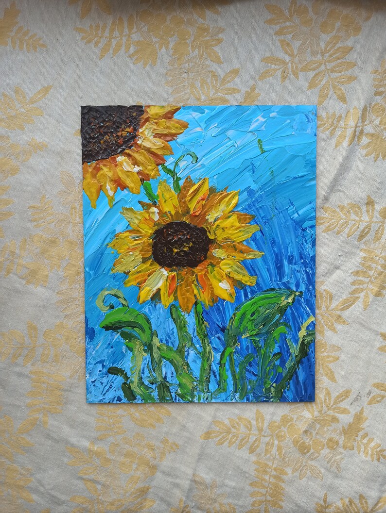 K&ouml;nnte beinhalten: Ein Gem&auml;lde von zwei Sonnenblumen mit gelben Bl&uuml;tenbl&auml;ttern und braunen Zentren vor einem blauen Hintergrund. Die Sonnenblumen sind mit dicken Farbschichten gemalt, was ihnen ein strukturiertes Aussehen verleiht.