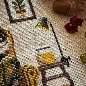 Detailed embroidery view of a steaming cup of tea on a small table next to the badger’s chair. A vintage desk lamp casting warm light over the badger’s reading corner.
