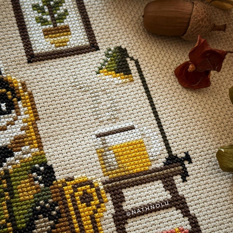 Detailed embroidery view of a steaming cup of tea on a small table next to the badger’s chair. A vintage desk lamp casting warm light over the badger’s reading corner.