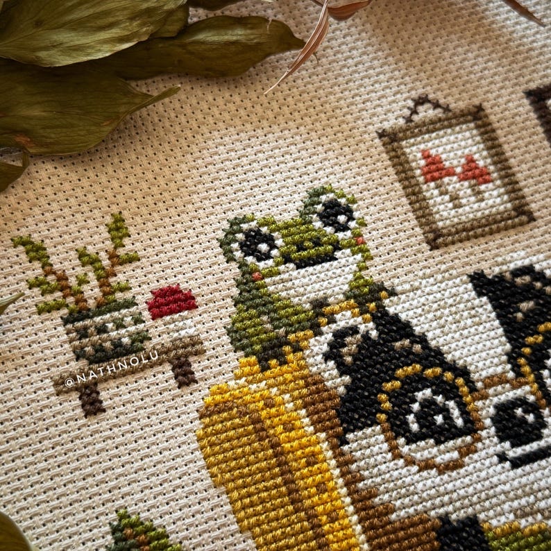 Close-up of a tiny frog sitting near the badger in the Reading Badger cross stitch design.