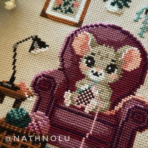 Close-up of crocheting mouse embroidery design holding yarn and hook in a warm farmhouse style craft room