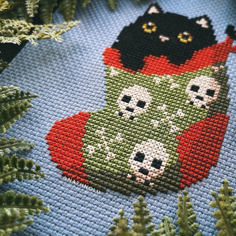 May include: A black cat peeking out of a green and red stocking with white skulls. The stocking is on a blue background.