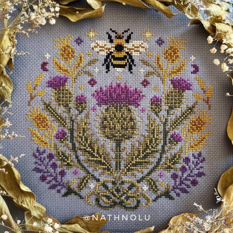 Thistle and bee cross stitch pattern featuring a bumblebee surrounded by blooming wild thistle flowers in a symmetrical botanical sampler