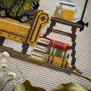 Library-inspired cross stitch design of a badger reading in a cozy armchair with vintage woodland charm.
