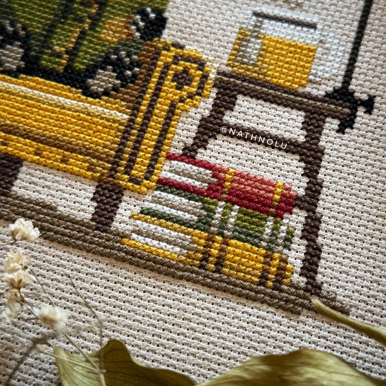 Library-inspired cross stitch design of a badger reading in a cozy armchair with vintage woodland charm.