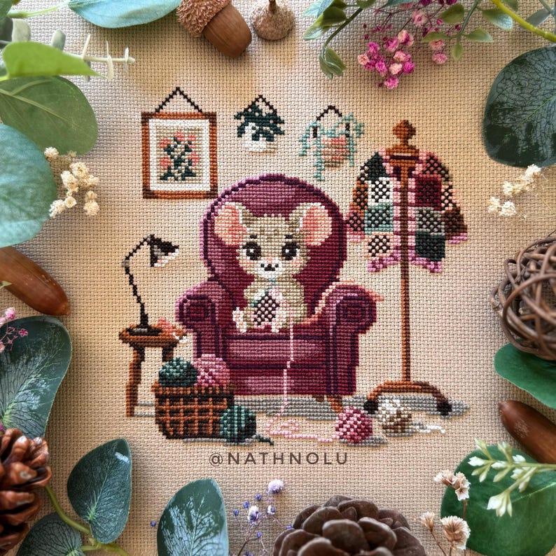 Crocheting mouse cross stitch pattern featuring a cute little mouse making granny squares in a cozy purple armchair