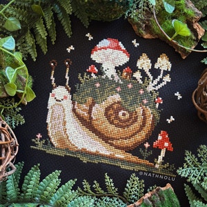 Könnte beinhalten: Kreuzstichmuster eines Schnecken mit einem Pilz auf dem Rücken. Die Schnecke ist braun und weiß, und der Pilz ist rot und weiß. Der Hintergrund ist schwarz mit kleinen weißen Sternen.