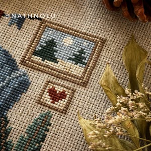 Close-up of elements from a cross-stitch pattern of a sewing fox. Pictures with winter forest scenes and heart embroidery.