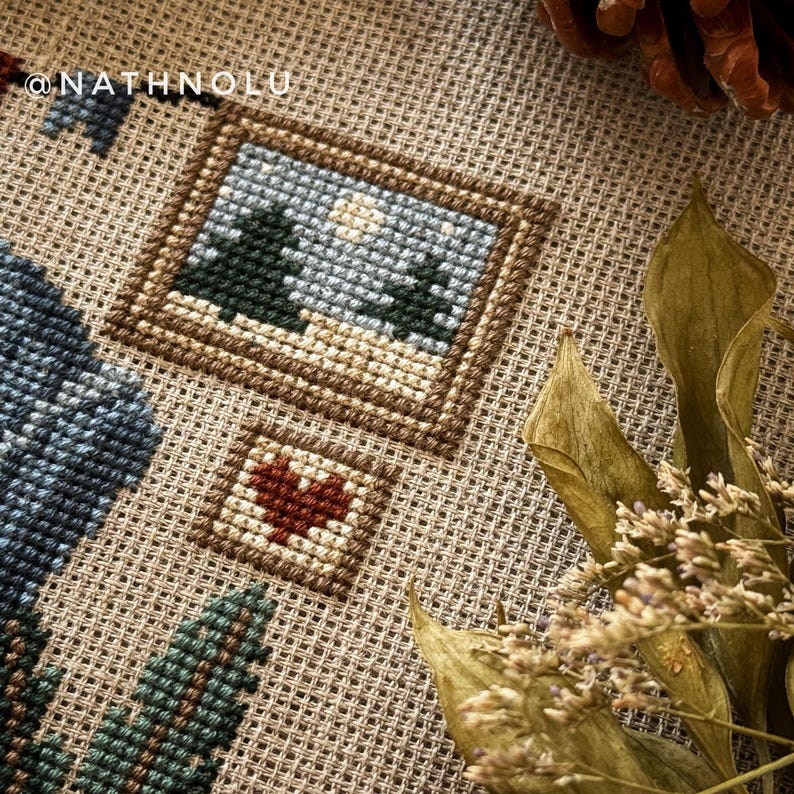 Close-up of elements from a cross-stitch pattern of a sewing fox. Pictures with winter forest scenes and heart embroidery.
