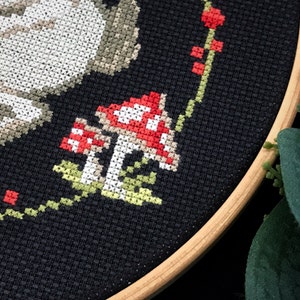 A fragment of a plant wreath embroidery by cross in the middle of which are fly agaric