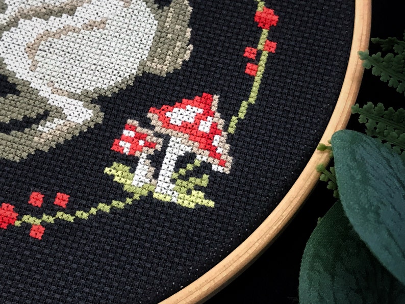A fragment of a plant wreath embroidery by cross in the middle of which are fly agaric