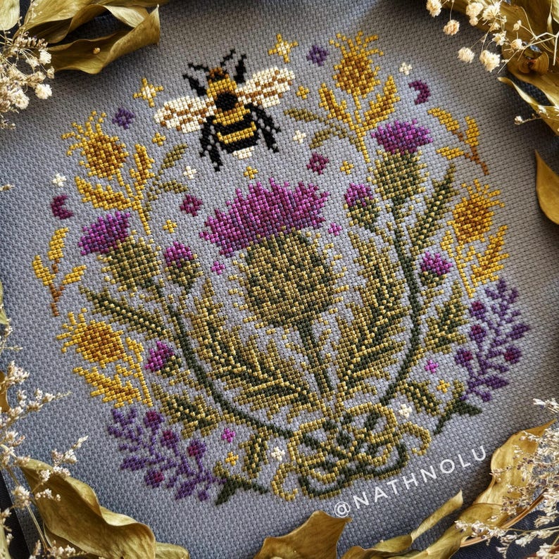 Botanical cross stitch design with purple thistle flowers and a bee, inspired by wildflower meadows and cottagecore decor.