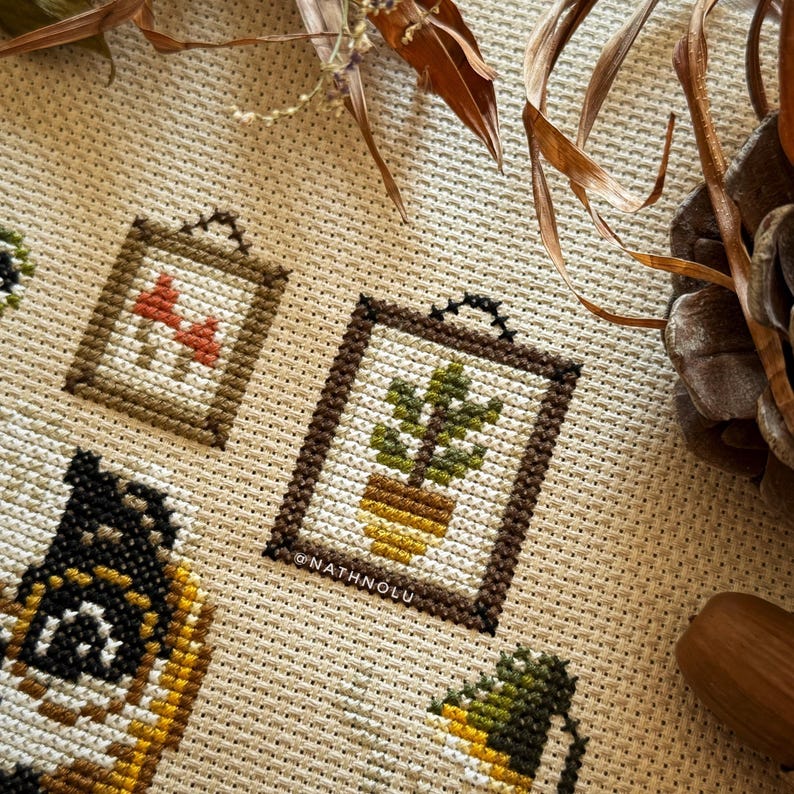 Wall decor details from the Reading Badger cross stitch design showing framed pictures of plants and mushrooms.