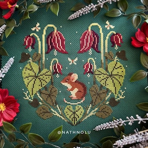 Könnte beinhalten: Kreuzstichmuster mit einer braunen Maus, roten Blumen, grünen Blättern und Schmetterlingen auf einem tealfarbenen Hintergrund. Das Design wird von roten Blumen und grünen Blättern umrahmt. Der Text "@NATHNOLU" befindet sich unten.