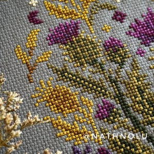 Detailed flower cross stitch showing purple thistle blooms and a realistic bee in a balanced ornamental layout.