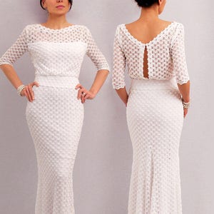 May include: A white, two-piece, crochet dress. The top has three-quarter sleeves and a boat neck. The skirt is a fitted, floor-length design with a slight flare at the bottom. The back of the top has a keyhole opening. The dress is made of a textured, open-weave fabric.
