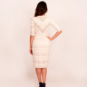 May include: Cream-coloured lace dress with a fitted shape and elbow-length sleeves. The dress has a detailed lace pattern on the bodice and skirt. The model is wearing navy blue high heels. Suitable for formal occasions.