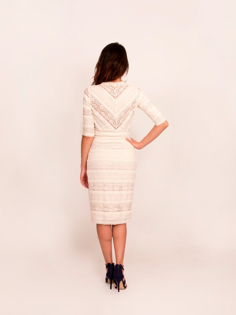May include: Cream-coloured lace dress with a fitted shape and elbow-length sleeves. The dress has a detailed lace pattern on the bodice and skirt. The model is wearing navy blue high heels. Suitable for formal occasions.