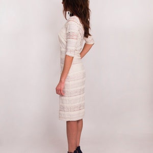 May include: Ivory lace dress with three-quarter sleeves and a knee-length skirt. The dress features a detailed lace pattern and is paired with navy blue strappy heels.