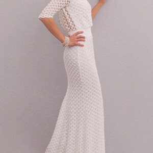 May include: A white, textured, floor-length dress with a matching bolero jacket. The dress features a fitted bodice and a flared skirt. The bolero has three-quarter sleeves. A pearl bracelet adorns the wrist. The dress is made of a delicate, open-weave fabric.