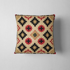 May include: Square throw pillow with a geometric pattern. The pillow features a tan background with a repeating design of black, red, and gold shapes. The edges are trimmed with a black border and red corner accents.