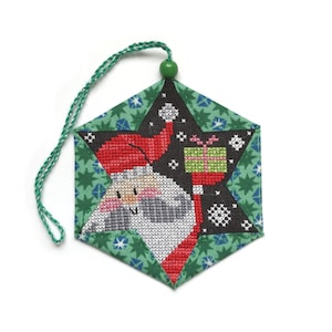 May include: A green, red and white star-shaped Christmas bauble with a stitched image of Santa Claus holding a gift. The bauble has a green string for hanging.