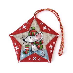 May include: A star-shaped Christmas ornament with a red border and a stitched design of a mouse wearing a hat and scarf, carrying a stocking. The ornament has a red and gold hanging cord.