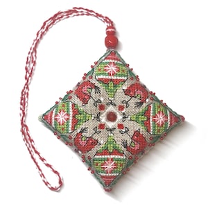 Pode incluir: Um enfeite de Natal quadrado com um design vermelho, verde e branco. O enfeite é feito de tecido e tem uma borda de contas. Tem um cordão vermelho e branco para pendurar.