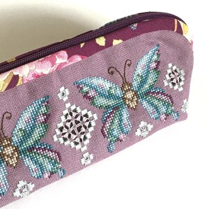 May include: A purple fabric pencil case with a floral design and embroidered butterflies. The butterflies are in shades of blue, green, and brown.