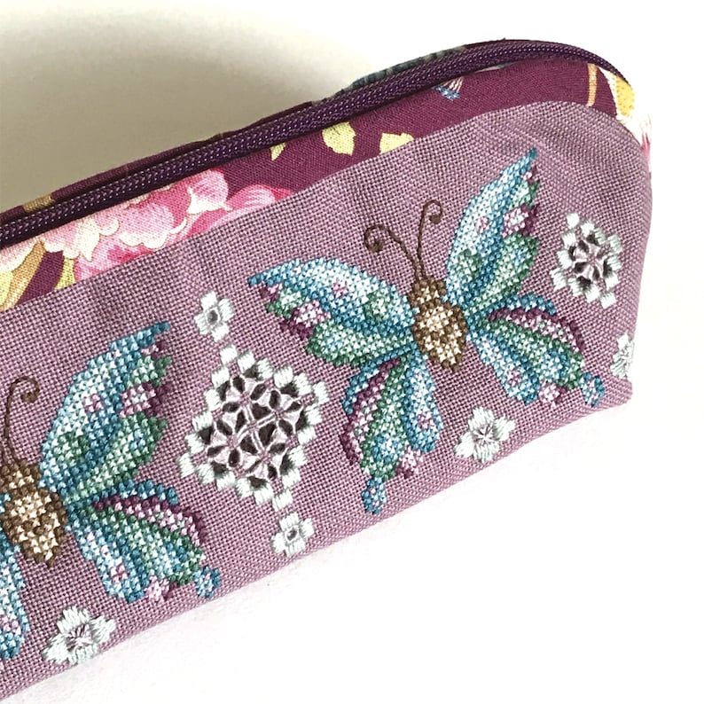 May include: A purple fabric pencil case with a floral design and embroidered butterflies. The butterflies are in shades of blue, green, and brown.