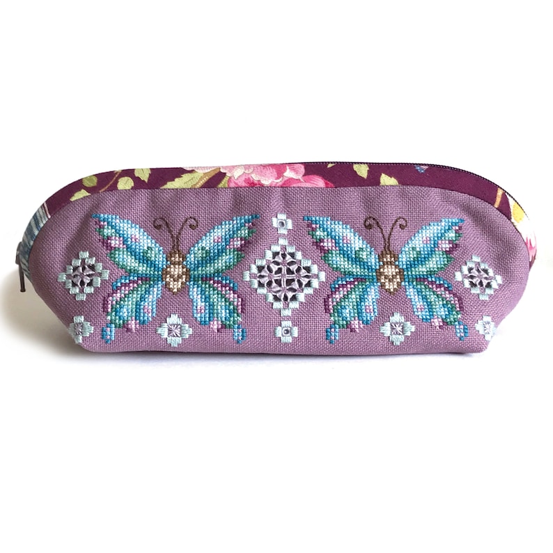 May include: A lavender-colored zippered pouch with a floral print on the top and two embroidered butterflies on the front. The butterflies are blue, green, and brown.