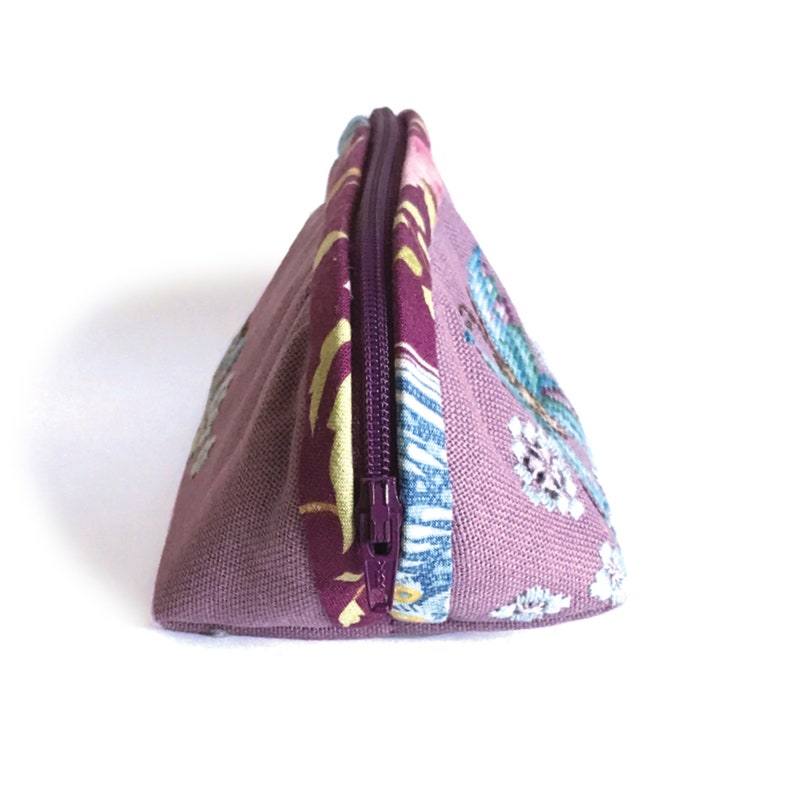 May include: A purple zippered pouch with a floral pattern. The pouch is made of fabric and has a purple zipper.