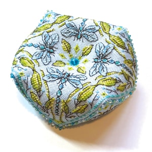 Può includere: Un ferma-ago blu e verde con un design a libellula e un bordo di perline.