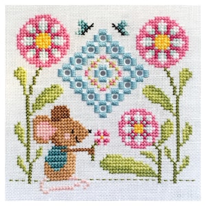 Op de afbeelding: Kruissteekontwerp met een bruine muis die een roze bloem vasthoudt, omringd door roze en witte bloemen, groene bladeren en een blauw en wit ruitpatroon. Twee kleine blauwe insecten bevinden zich boven de ruit. Het ontwerp staat op een witte achtergrond.