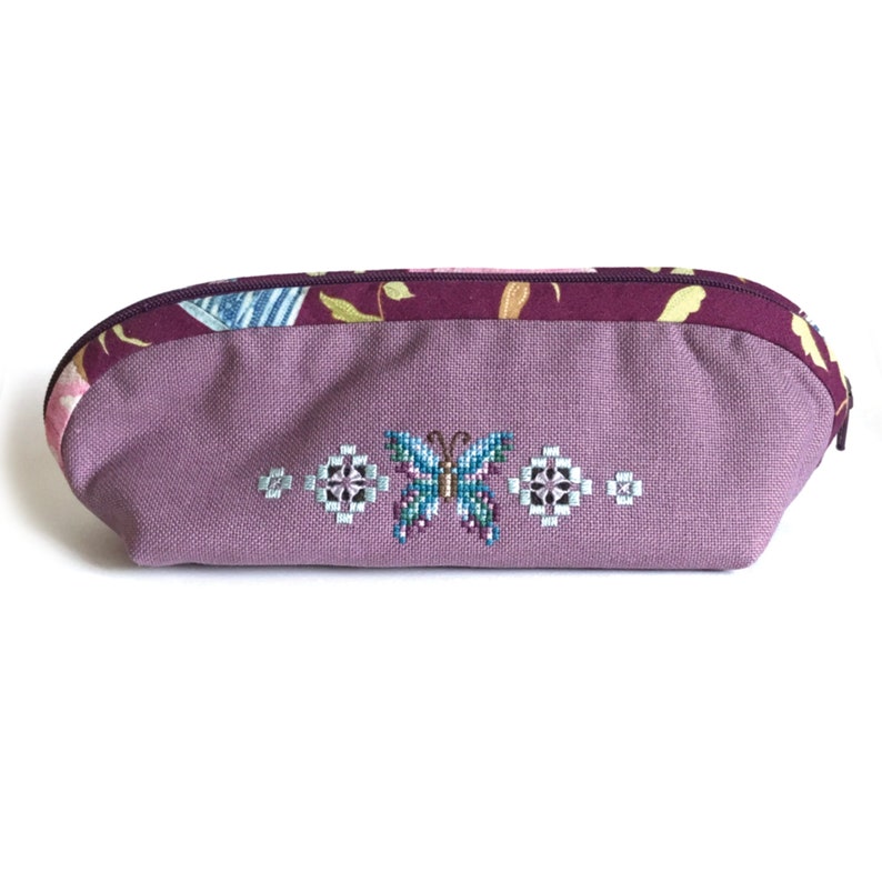 May include: A purple zippered pouch with a butterfly embroidered on the front. The pouch has a burgundy floral fabric lining.