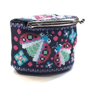 May include: A black coin purse with a silver clasp. The purse is decorated with a colorful embroidered design of butterflies and flowers.
