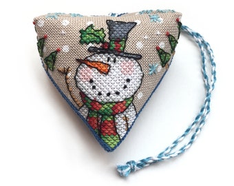 Könnte beinhalten: Ein herzförmiger Anhänger mit einem Schneemann-Motiv. Der Schneemann trägt einen grün-rot-weißen Schal und einen schwarzen Zylinder. Der Anhänger hat eine blaue und weiße Schnur.