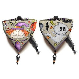 Könnte beinhalten: Zwei reversible Halloween-Hundehalstücher mit schwarzem und orangefarbenem Besatz. Eine Seite zeigt eine Comic-Hexe mit einem lila Hut und orangefarbenen Haaren. Die andere Seite zeigt ein weißes Gespenst mit schwarzen Augen und einem schwarzen Mund. Beide Halstücher haben einen schwarzen Quasten.